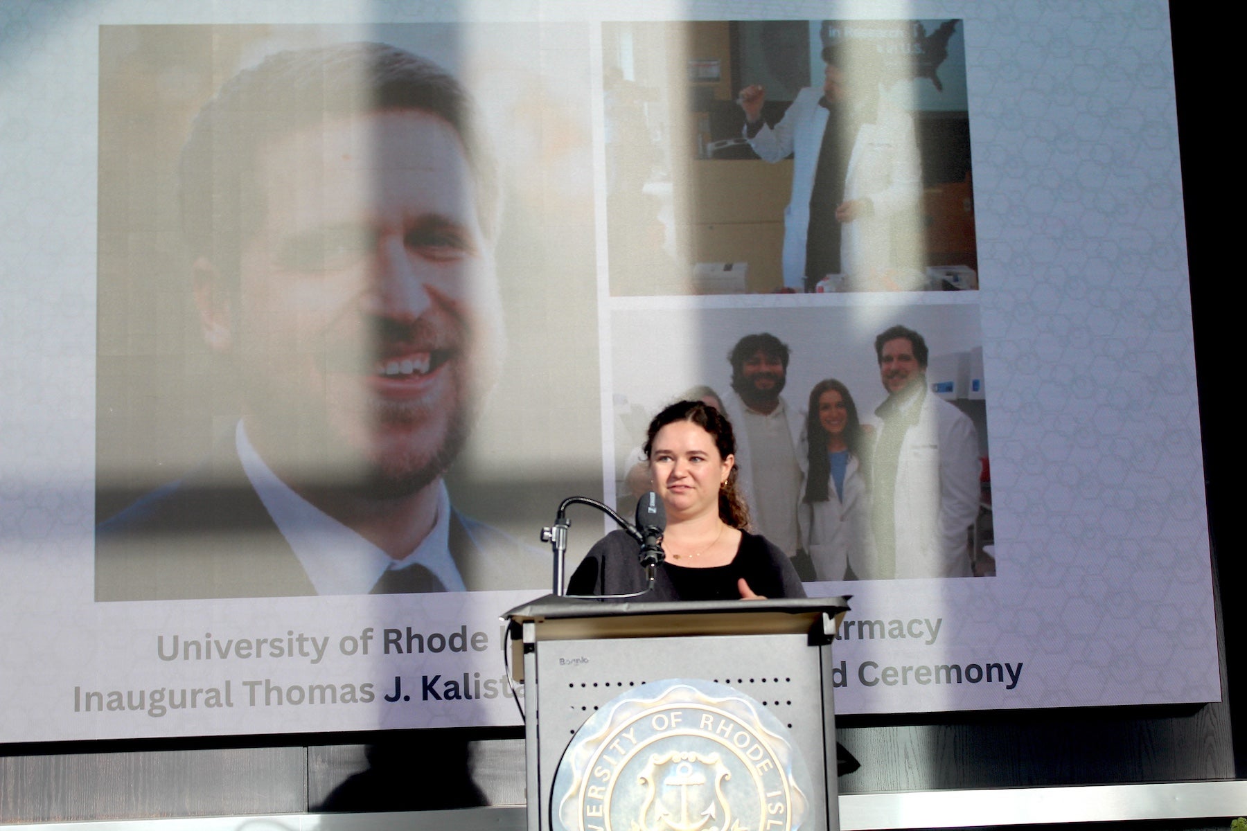 Doctor of Pharmacy student Cailin McCaffrey accepts the inaugural Thomas J. Kalista Scholarship in front of a video board showing photos of the late professor for whom the scholarship is named.
