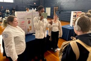 URI College of Pharmacy student Shakir Spike blocks his mouth so South Kingstown High School students can't read his lips as he tests their hearing age during an interactive health and wellness fair at the High School on Dec. 5.