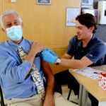 Student Jason Cambra delivers the COVID vaccine to Pharmacy Dean Paul Larrat.