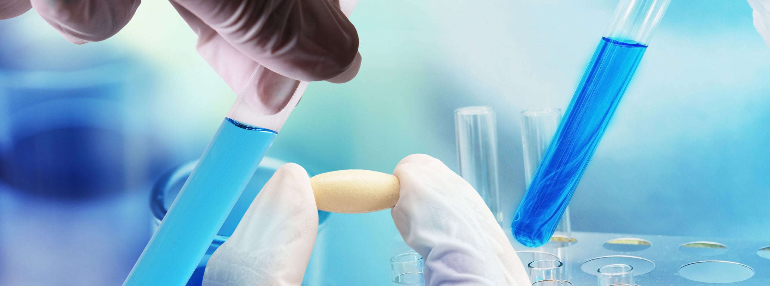gloved hands holding a pill and test tube