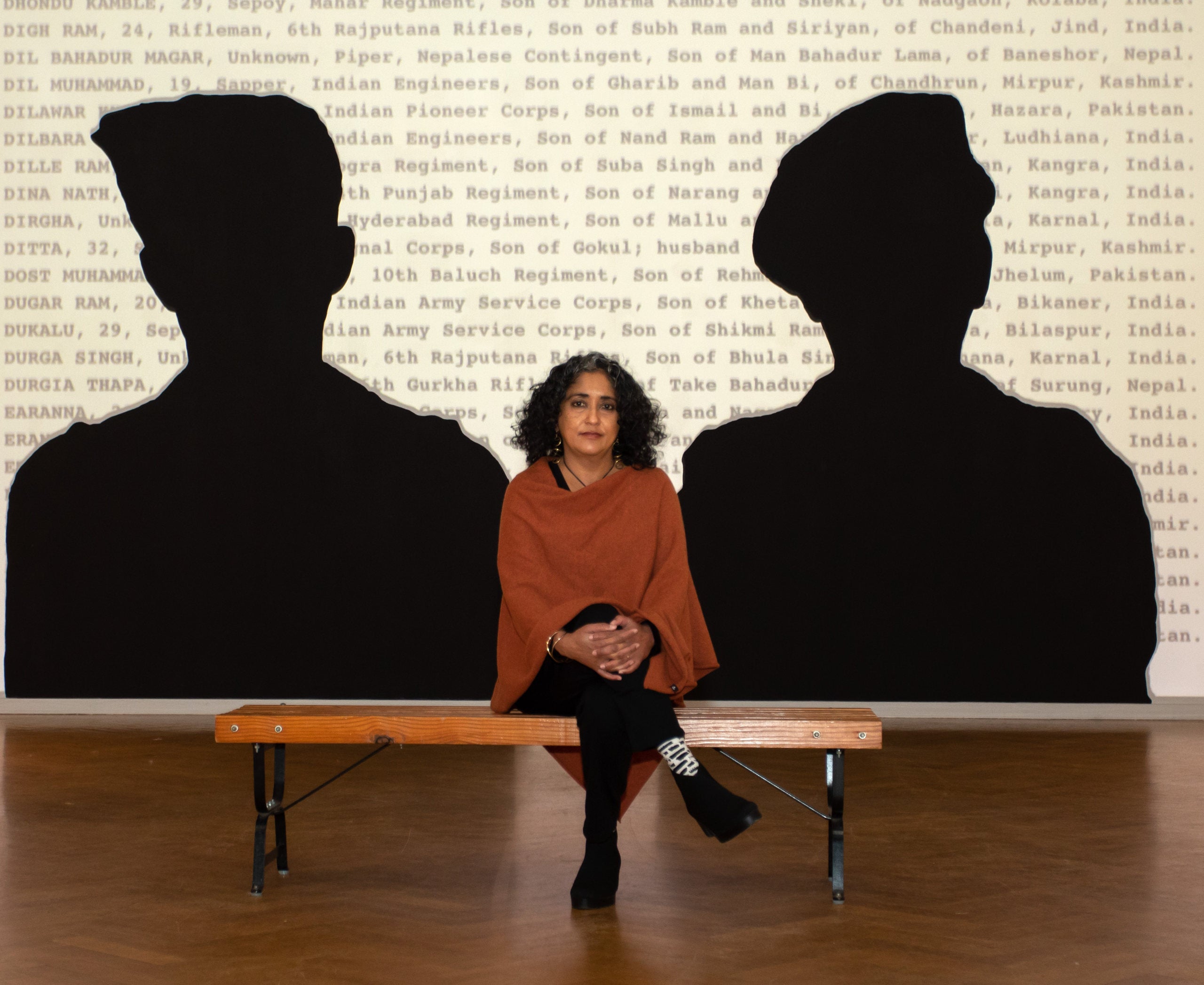 URI photography professor Annu Palakunnathu Matthew, seated in a gallery in front of one of her silhouetted artworks