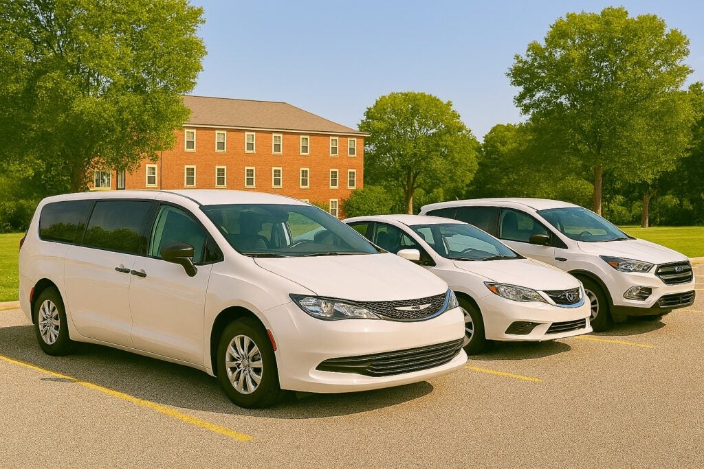 Three white passenger vehicles parked outdoors near a building and trees.