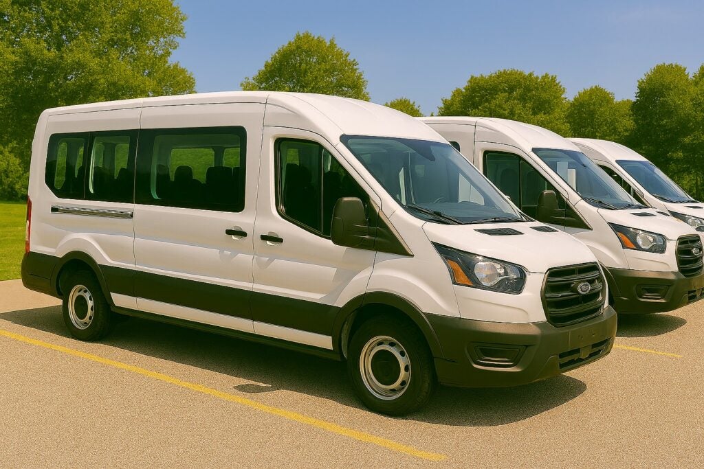Three white passenger vans parked outside near trees.