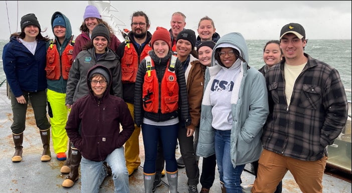 Scientists on a ocean research cruise pose for a photo on the deck of their research vessel.