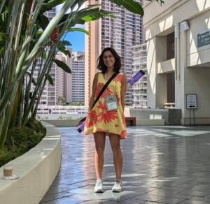 Photo of lab member Sabine standing in the shade of a tropical plant with a poster tube slung over her shoulder.