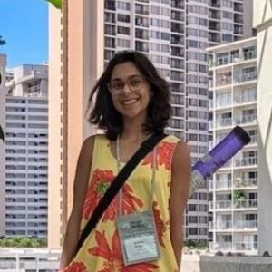 Photo of lab member Sabine standing in the shade of a tropical plant with a poster tube slung over her shoulder.
