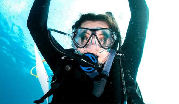 a woman scuba diving underwater with goggles and breathing equipment on and her arms up