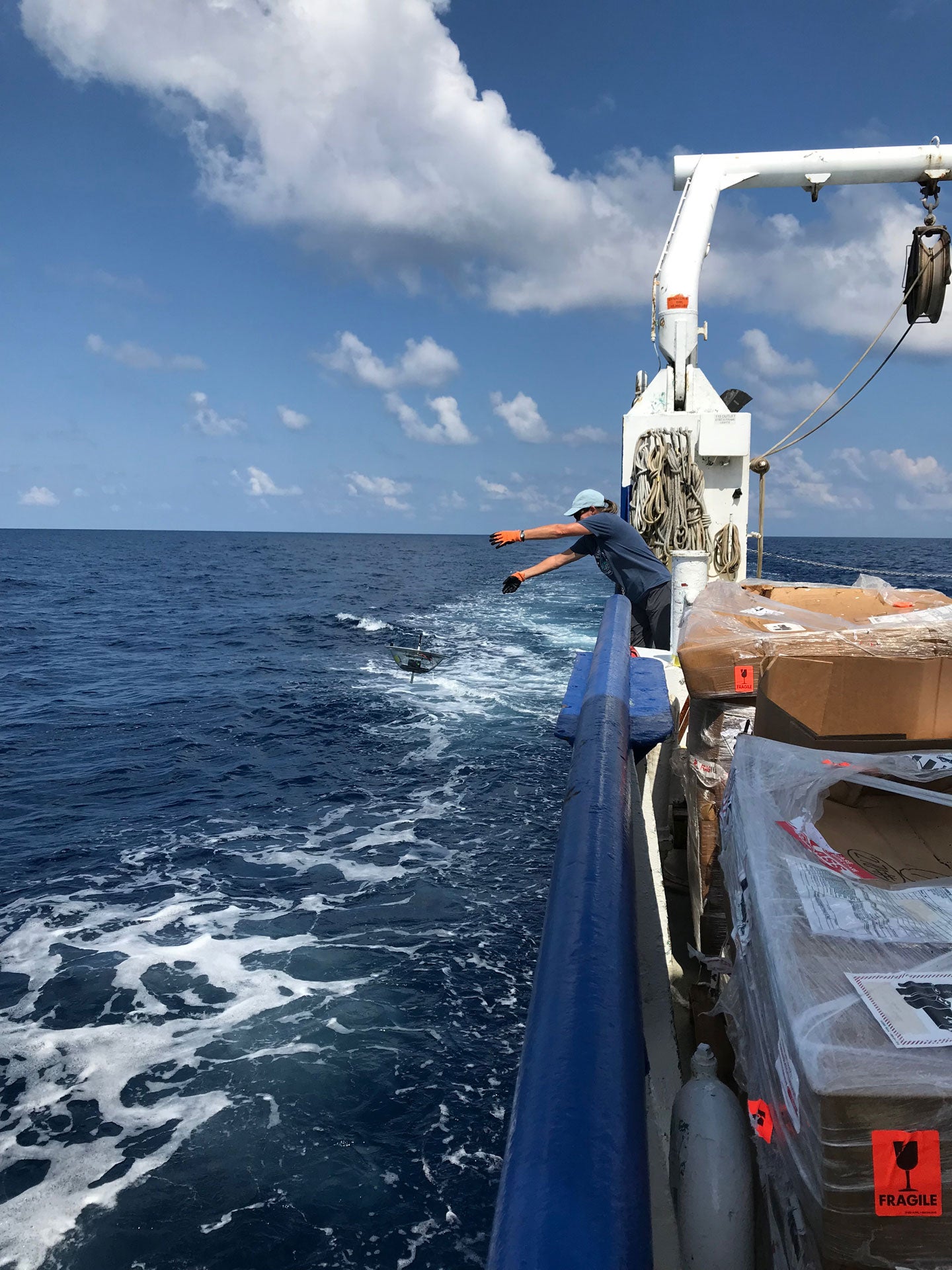 A researcher tosses a round disc into the ocean, a drifter that was deployed on behalf of DARPA.