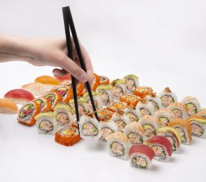 Chopsticks picking up sushi roll from a platter