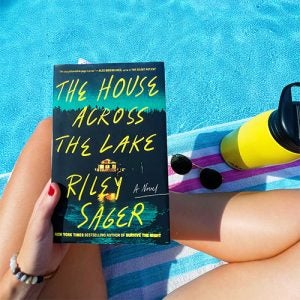 tara reading the house across the lake, poolside with sunnies and a yellow water bottle in the top right corner