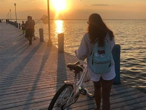 girl walking her bike down a boardwalk at sunset, there are fishermen in the foreground