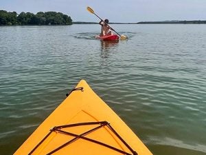 kayaking on lake, picture taken from a yellow kayak with guy paddeling toward camera 