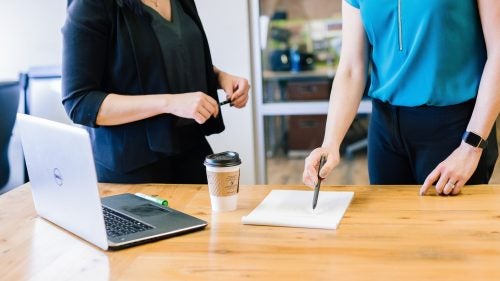 Two women discussing work while pointing to a notepad