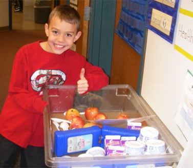 child smiling next to healthy foods