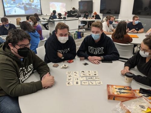 Several students sitting at tables playing board and video games together