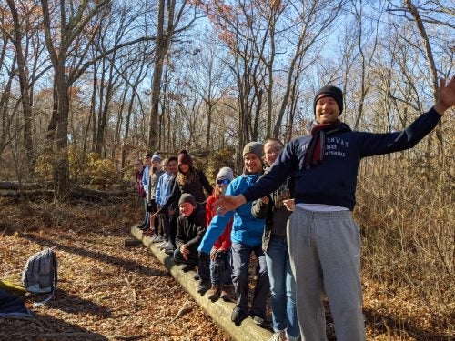 A group of students balance on a wooden beam during an outdoor challenge course