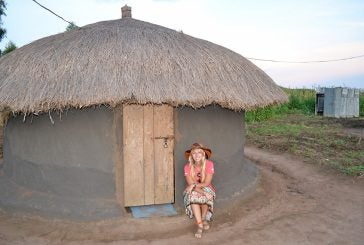 Kayla Kurtz in front of clay hut in Uganda