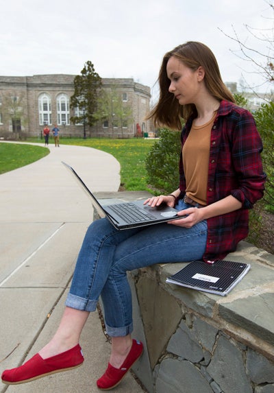 Julia Santini sitting with her laptop on the URI campus