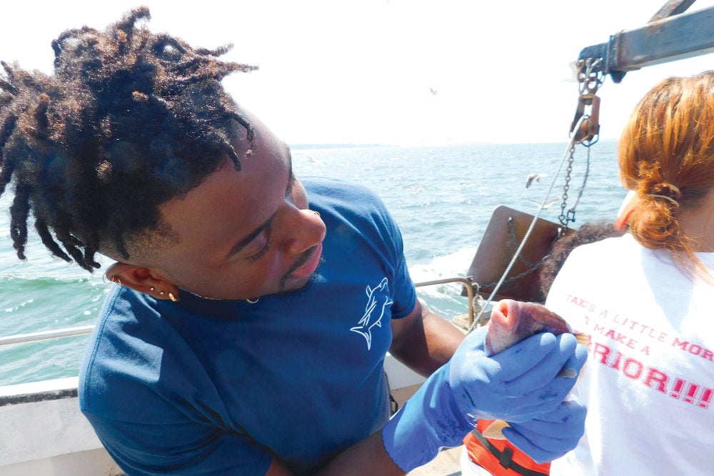 Gyasi Alexander inspects a fish on board a boat during URI's 2018 Summer Shark Camp for high school students, which he helped coordinate.