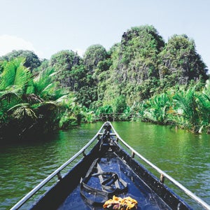 A boat wends through the waters surrounding dramatic, vegetation-covered limestone formations in Rammang Rammang, South Sulawesi, Indonesia.