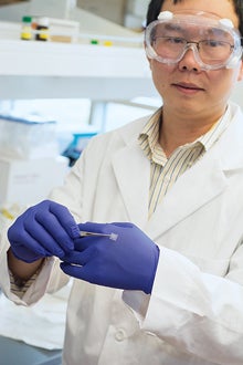 Xinyuan Chen, assistant professor of biomedical and pharmaceutical sciences, holds the patch next to a traditional hypodermic needle.