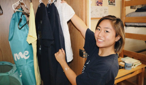 A student moves clothing into her dorm room.