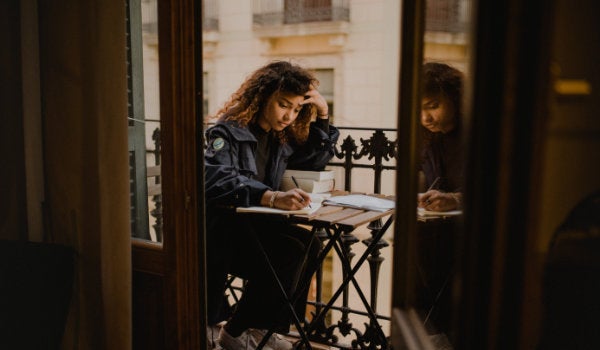 A woman seated on a balcony with a computer and paperwork