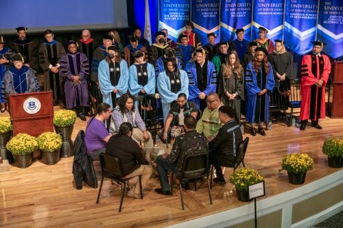 The Yootay Singers, featuring members of the Narragansett Indian Tribe, open the inauguration ceremonies on stage, surrounded by university leadership and other distinguished guests