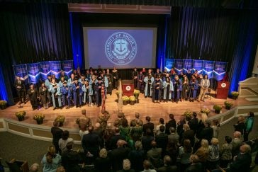 Wide shot of university leadership and other distinguished guests stand on stage