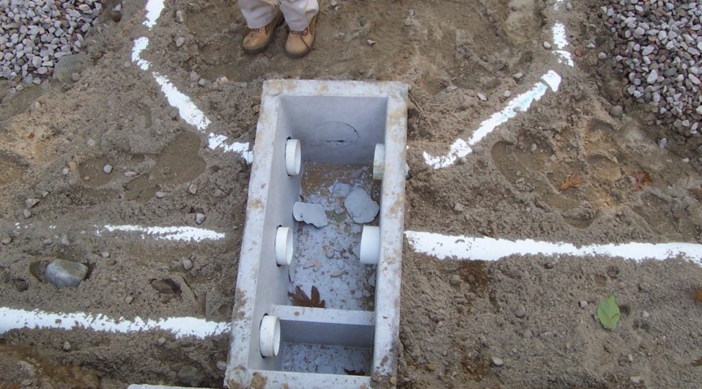 Photo of distribution box half buried showing inflowing line and 4 pipes exiting distribution box