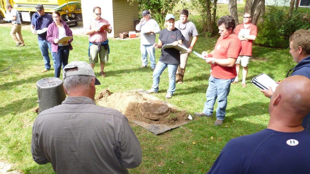 Group of participants around tarp and septic tank lid in outdoor training class