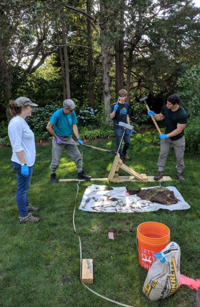 Researchers pounding a coring device into a drainfield in a shaded lawn