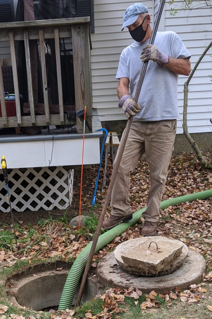 Gloved man holding long pole standing on hose pumping septic tank