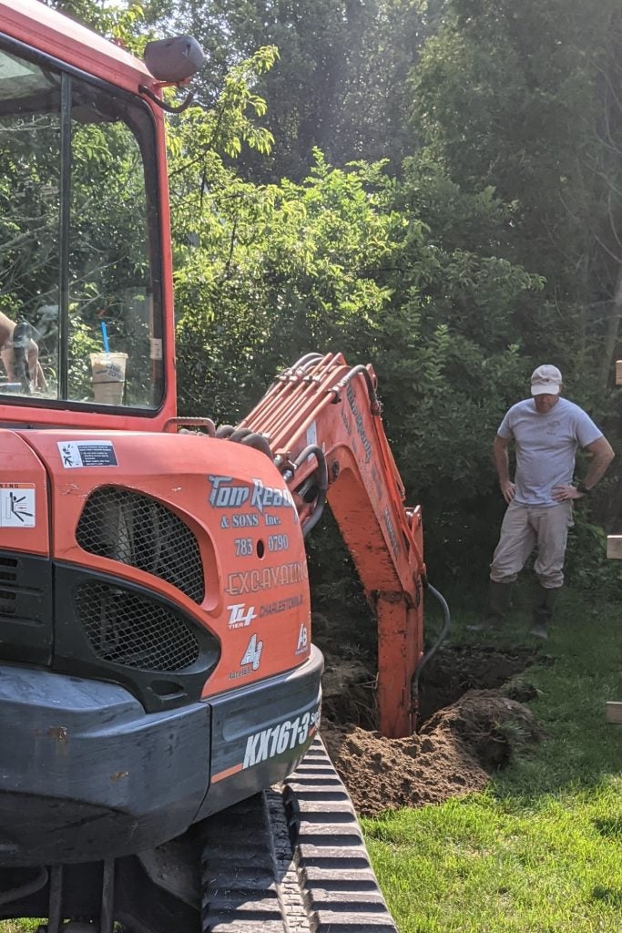 Person in background watching excavator dig hole
