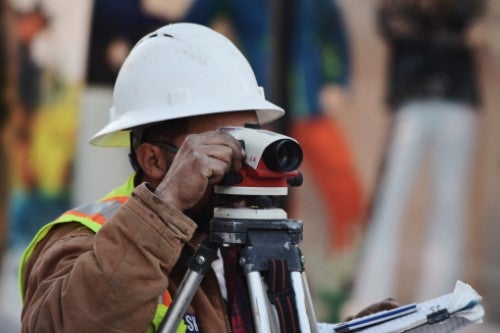 person in hard hat looking through laser level on tripod