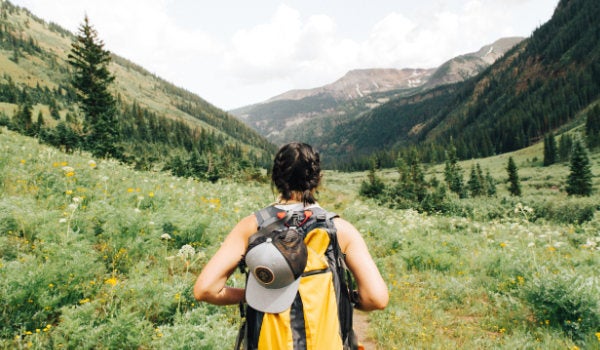 A hiker wearing a large backpack walking into a lush mountainous valley