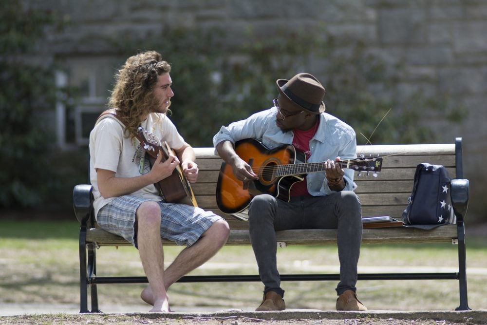 Two students playing guitar on a bench