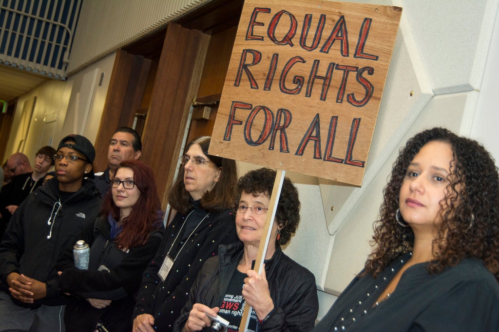 Several people standing in a hall. One holds a sign that reads equal rights for all