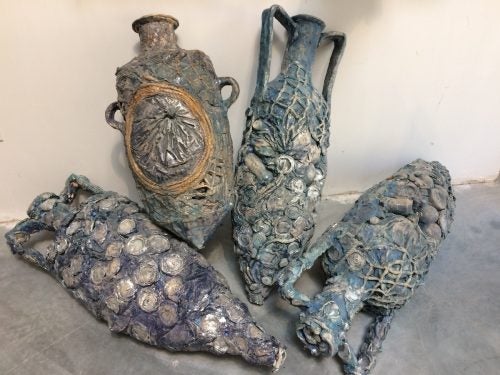 Four ancient-looking urns on the floor, they are blue-gray and appear to be covered in barnacles and mussels, they appear worn and old.