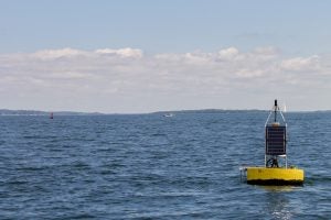 Photo of a yellow buoy station floating in Narragansett Bay.