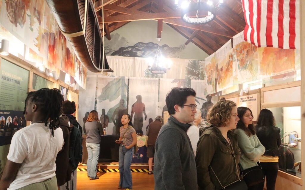 A photo of the main floor of the Tomaquag Museum. The room is full of people who are observing the various artifacts and signs that align the walls.